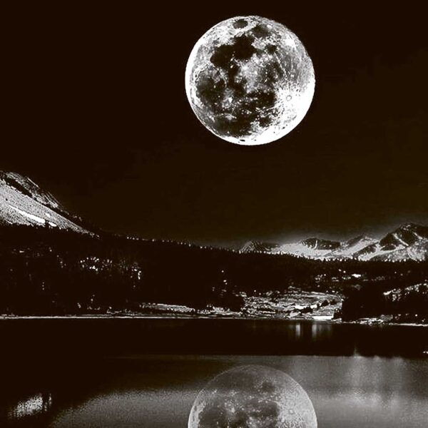 Stunning view of a full moon over a city by the lake, reflected in the water beneath snow-covered mountains at night.