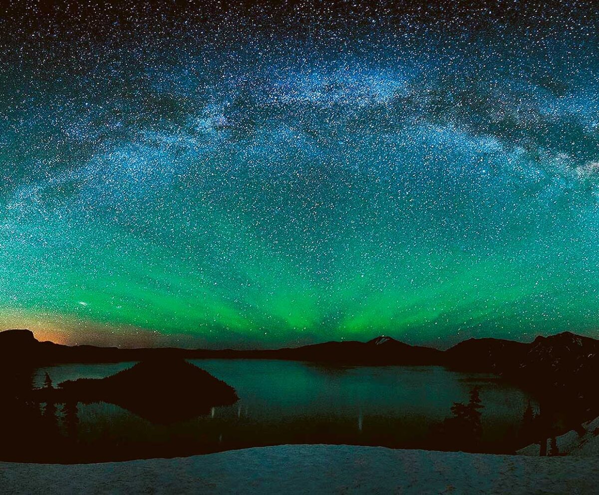 The Northern Lights (aurora borealis) stretching across a night sky with reflections over a still lake