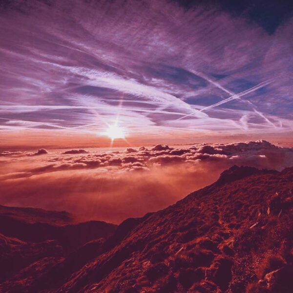 A sunrise emerging above the clouds over a mountain ridge, casting warm pink and orange hues across the sky