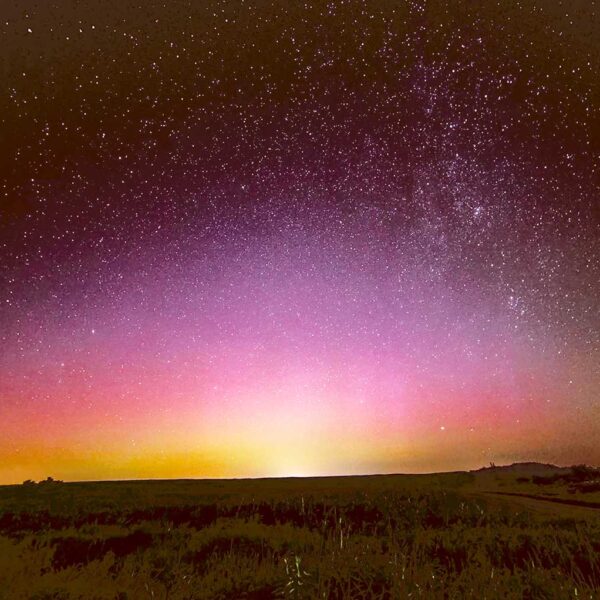 Northern lights glow softly over a vast horizon, fading from golden yellow to pink and purple under a star-speckled sky
