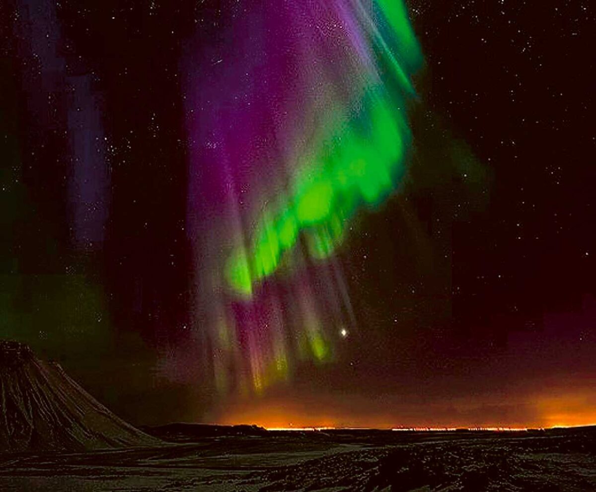 Vibrant aurora borealis with streaks of green and purple lighting up a starry sky above a mountainous horizon