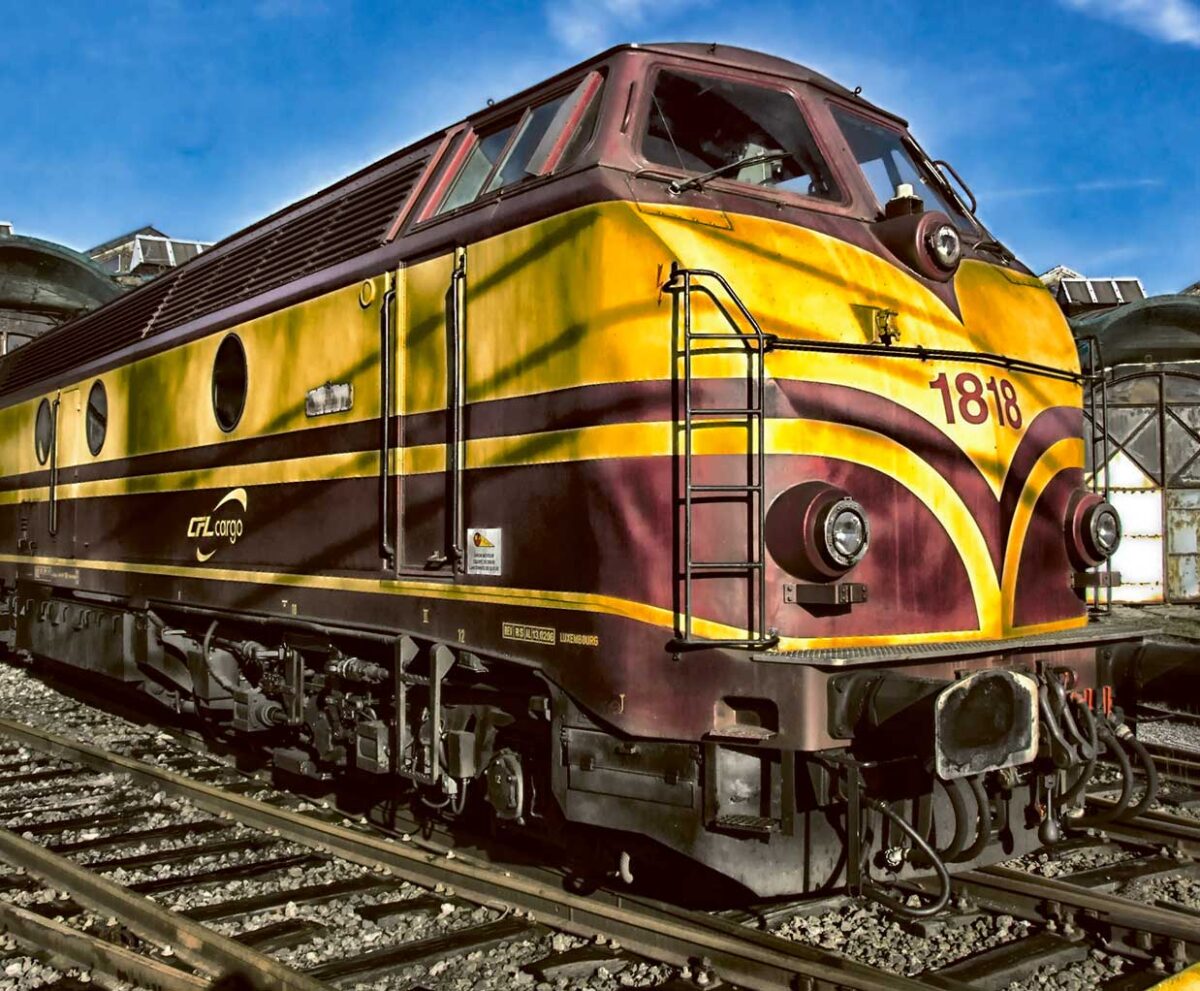 A vintage yellow and burgundy diesel locomotive labeled 1818, stationed on railway tracks under a bright blue sky.