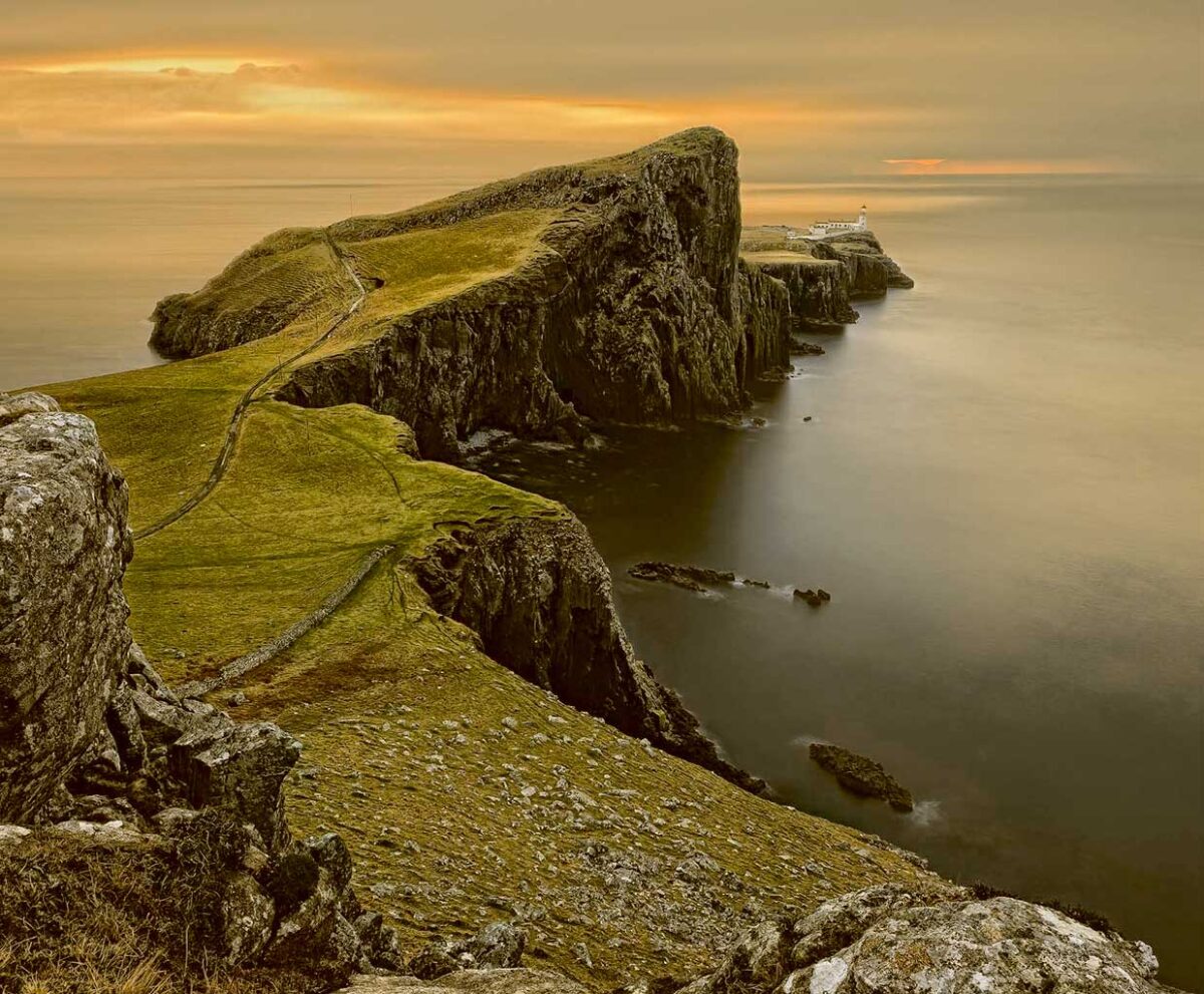 A dramatic cliffside view in Scotland with winding paths and a lighthouse at dusk